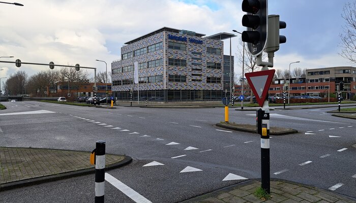 Een groot kruispunt met verkeerslichten voor auto's, voetgangers en fietsen. Op de achtergrond een modern gebouw met een kleurrijke gevel. 